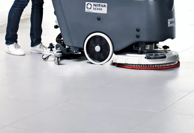auto floor scrubber being pushed by a person on a tile floor