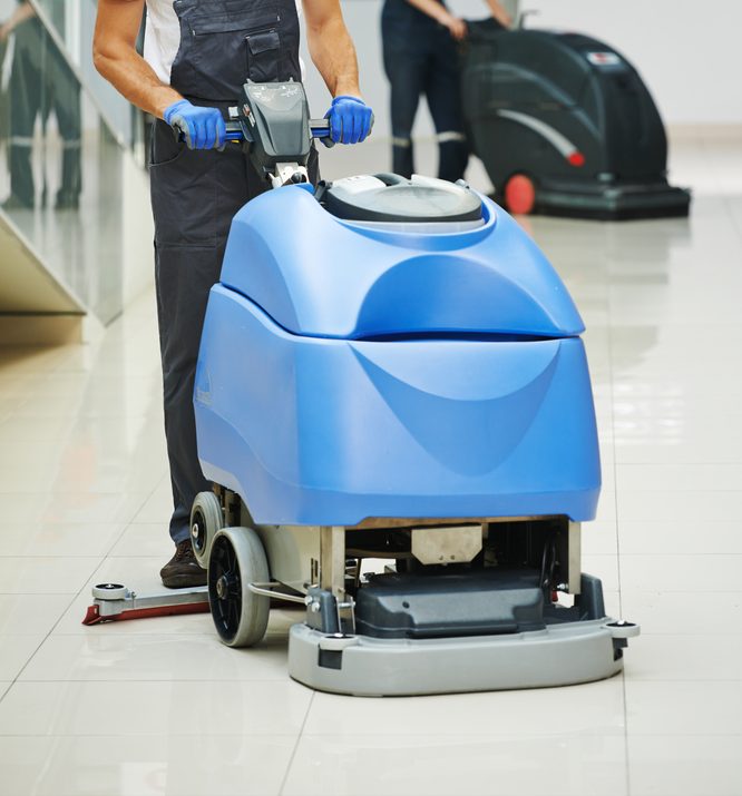 two pushable floor scrubbers in action on a business's floor